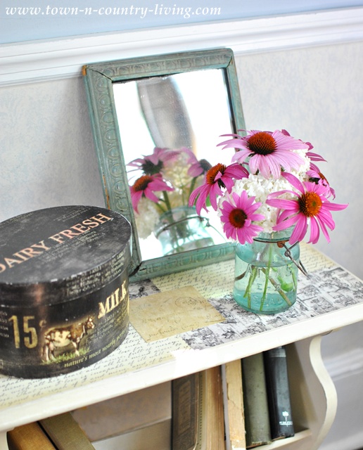 Summer flowers in a blue atlas jar atop a decoupaged end table via Town and Country Living