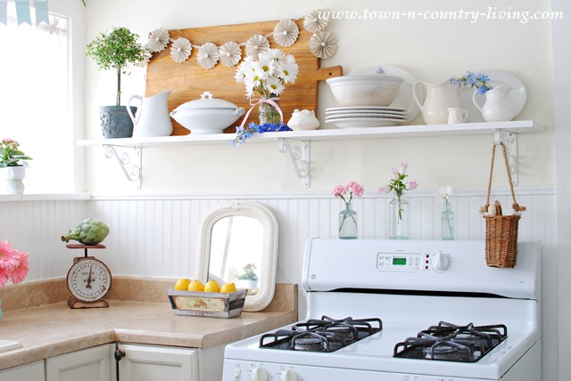 Open shelving features white ironstone and French bread board in farmhouse kitchen.