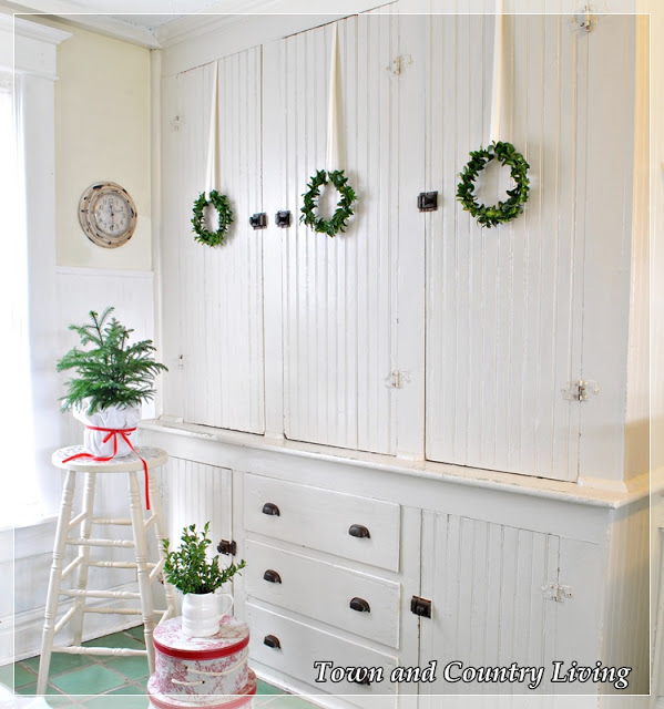 DIY Home Decor. A trio of boxwood wreaths adorns a built-in cupboard in an old farmhouse.