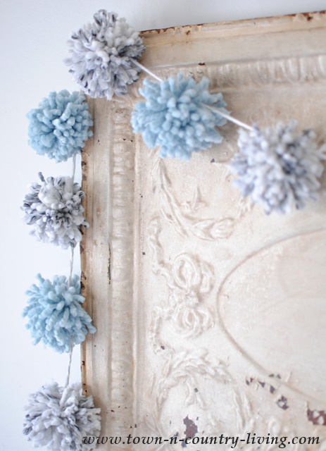 A pom pom garland in two colors of yarn soften a vintage ceiling tin. See how to make this garland for your own home decor.